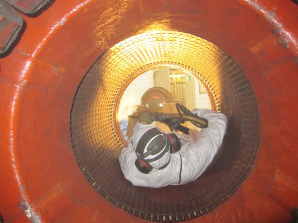 Person in Schutzkleidung, die orangenen Stator der hkw blumenthal GmbH von innen reinigt.